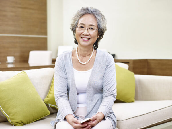 Senior woman wearing glasses sitting on couch smiling at camera
